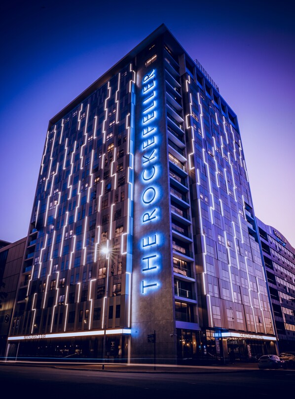 A modern hotel with a prominent vertical sign reading "THE ROCKEFELLER."