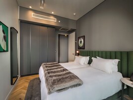 A modern hotel room with a large bed, a green upholstered headboard, a small bedside table, and a wall-mounted air conditioning unit.