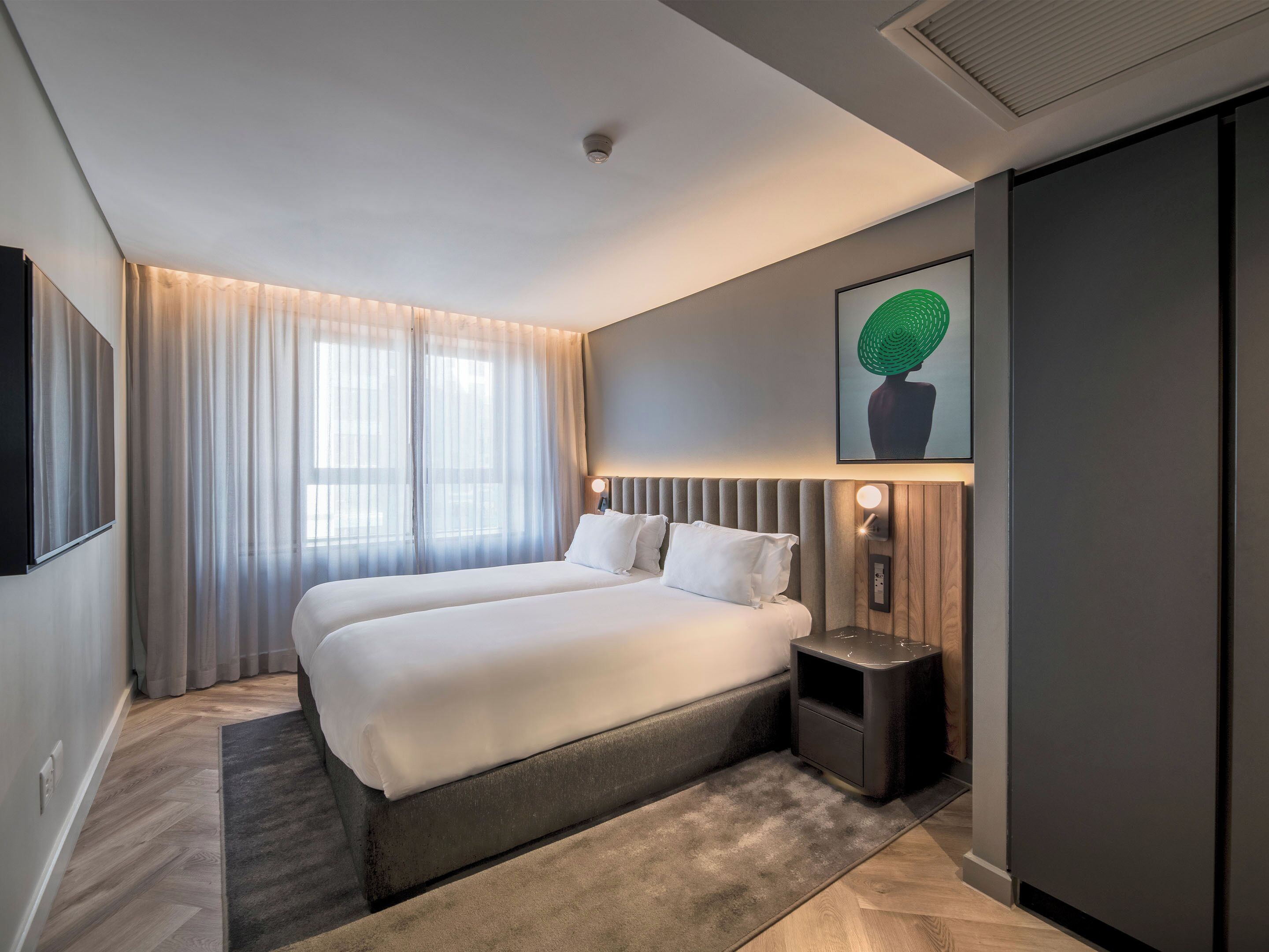 Une chambre d’hôtel moderne avec un grand lit, une table de chevet, un téléviseur fixé au mur et un luminaire au plafond.