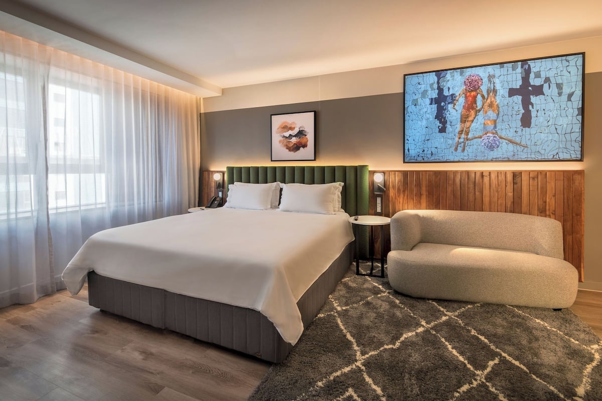 Ein modernes Hotelzimmer mit einem großen Bett, einem Nachttisch, einem Sessel und Bildern an der Wand.