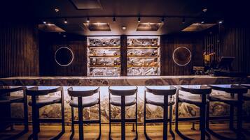 A bar area with marble countertops, stools, and shelves with bottles.