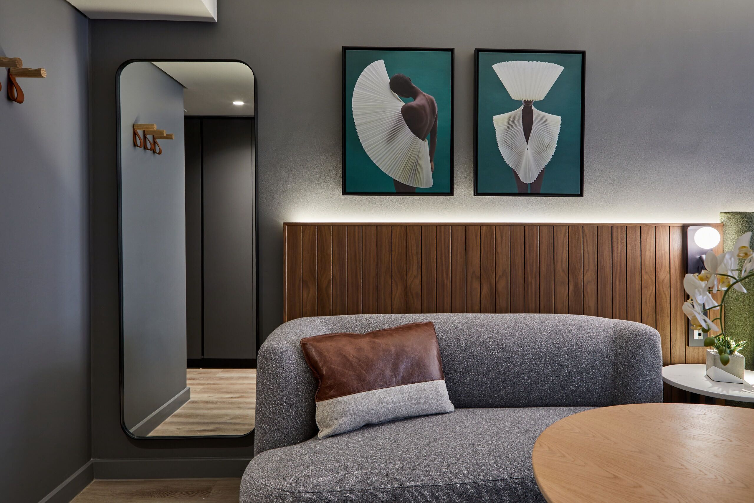 Ein modernes Wohnzimmer mit einem grauen Sofa, einem Holznachttisch und zwei gerahmten Kunstwerken an der Wand.