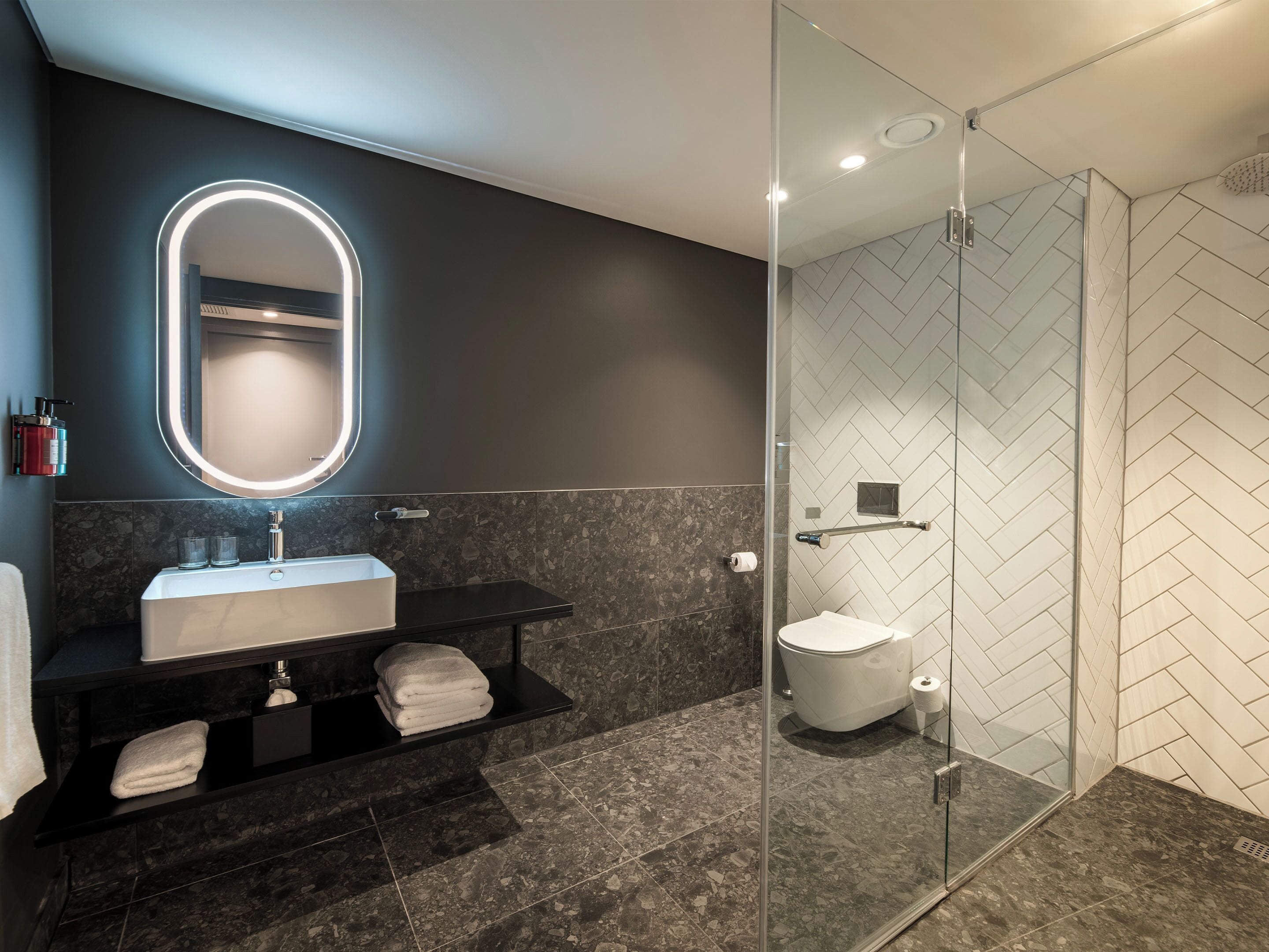 Een moderne badkamer met een glazen douchecabine, een wastafel met spiegel en een toilet.