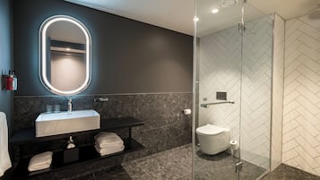Een moderne badkamer met een glazen douchecabine, een wastafel met spiegel en een toilet.