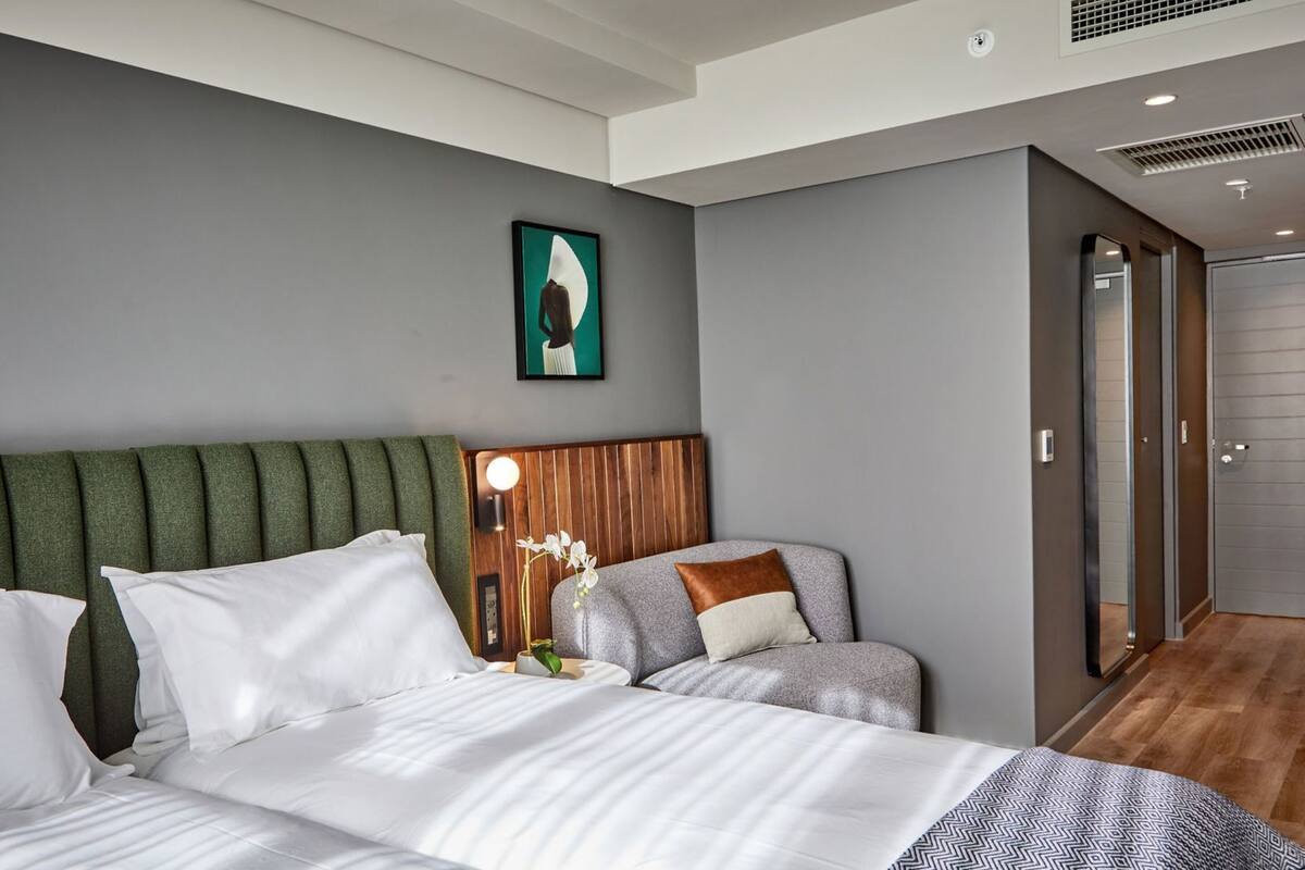 Ein modernes Hotelzimmer mit einem großen Bett, einem Holzkopfstütze, einem Nachttisch mit Lampe und einer Duschkabine.