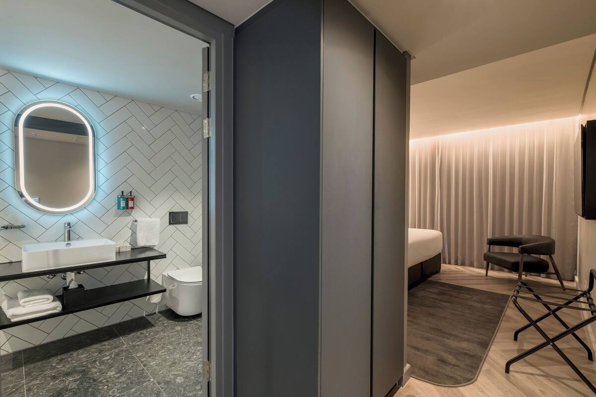 Ein modernes Badezimmer mit Fischschuppen-Fliesen an der Rückwand, einem großen Spiegel mit indirekter Beleuchtung, einem weißen Waschbecken und einer Toilette.