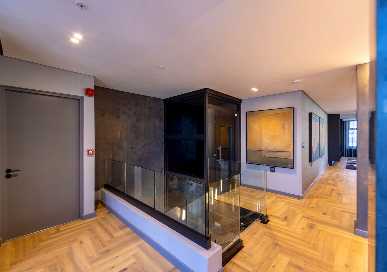 Un intérieur moderne avec une rambarde en verre, un plancher en bois et une porte dotée d’un signal lumineux rouge pour les situations d’urgence.