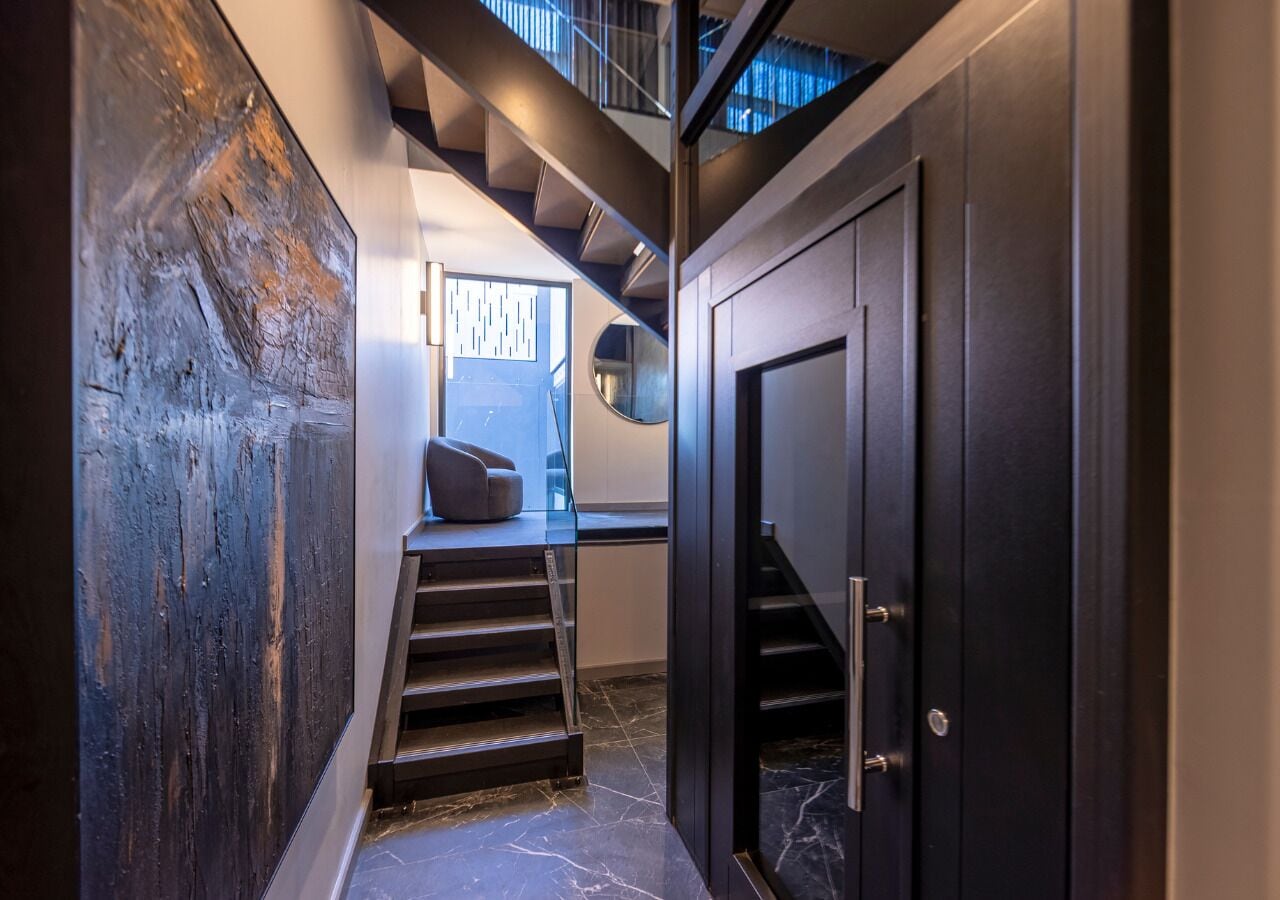 A modern interior with a staircase leading to a second floor, a dark door, and a textured wall.