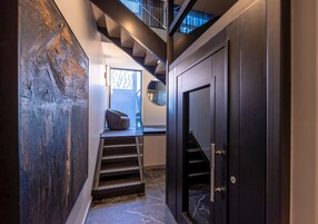 A modern interior with a staircase leading to a second floor, a dark door, and a textured wall.