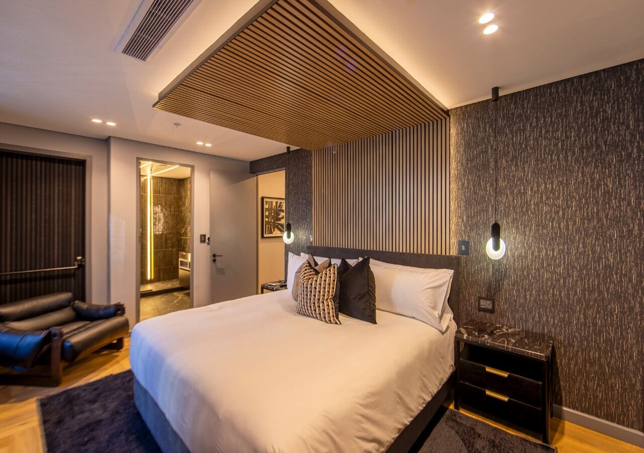A modern bedroom with a large bed, a seating area with a sofa, and a walk-in closet.
