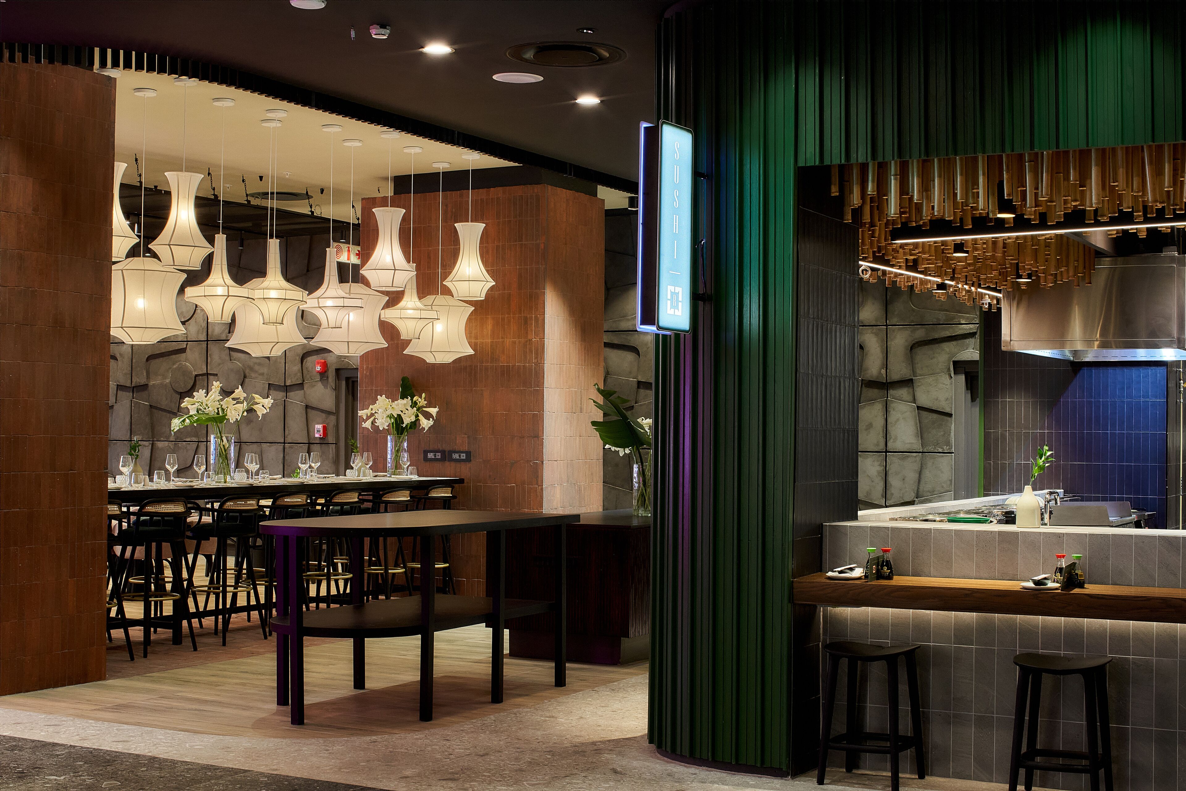 Un restaurante moderno con zona de bar, varias lámparas colgantes y un fondo de pared de piedra.