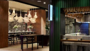 Un restaurante moderno con zona de bar, varias lámparas colgantes y un fondo de pared de piedra.