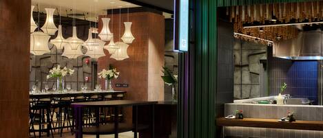 A modern restaurant with a bar area, multiple hanging light fixtures, and a stone wall backdrop.