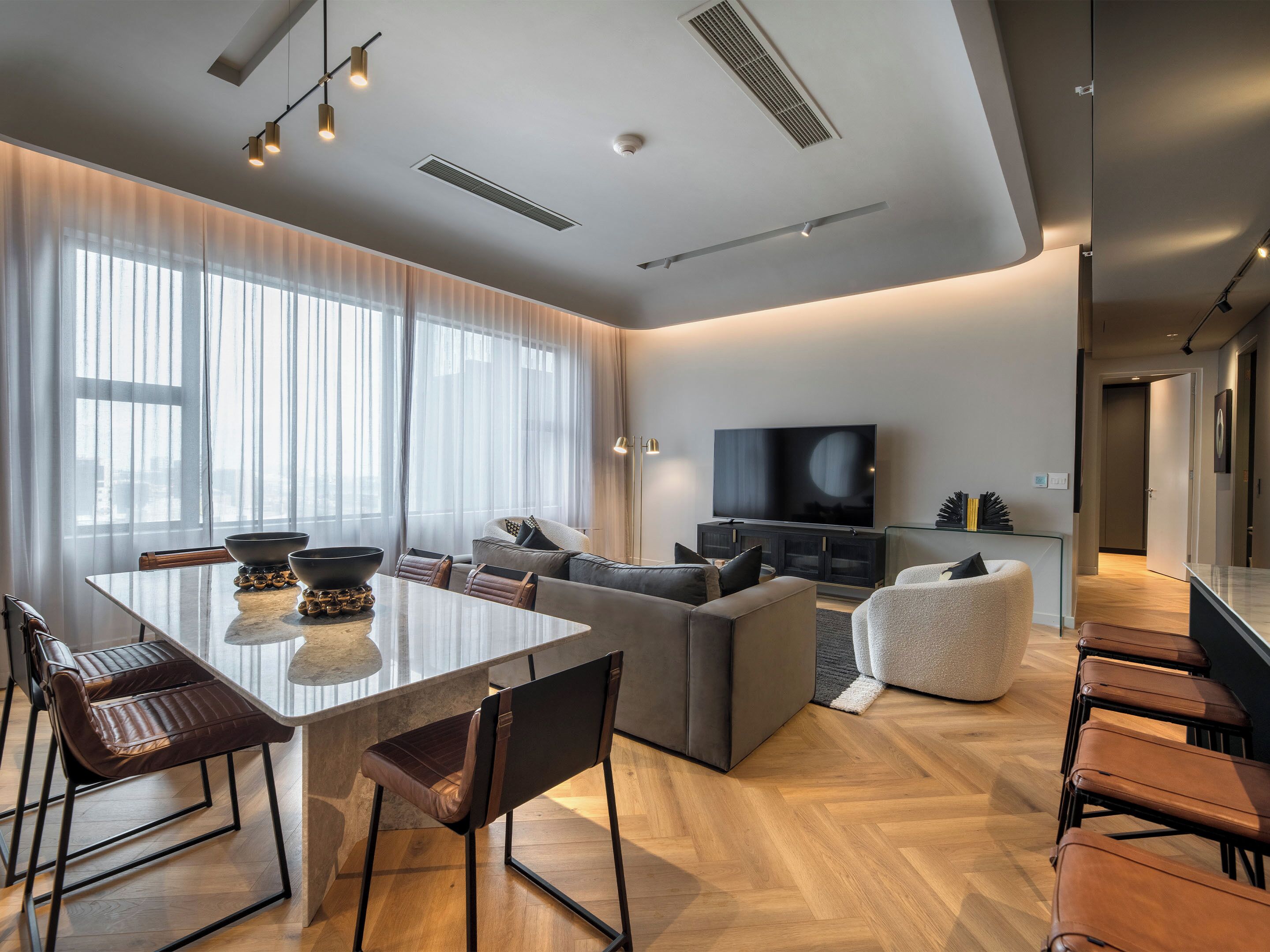 A modern living room with a dining area, a large flat-screen TV, and a view of the city through large windows.