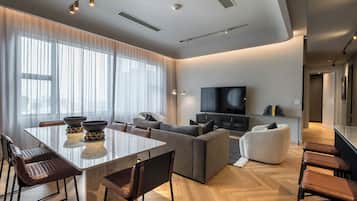 A modern living room with a dining area, a large flat-screen TV, and a view of the city through large windows.
