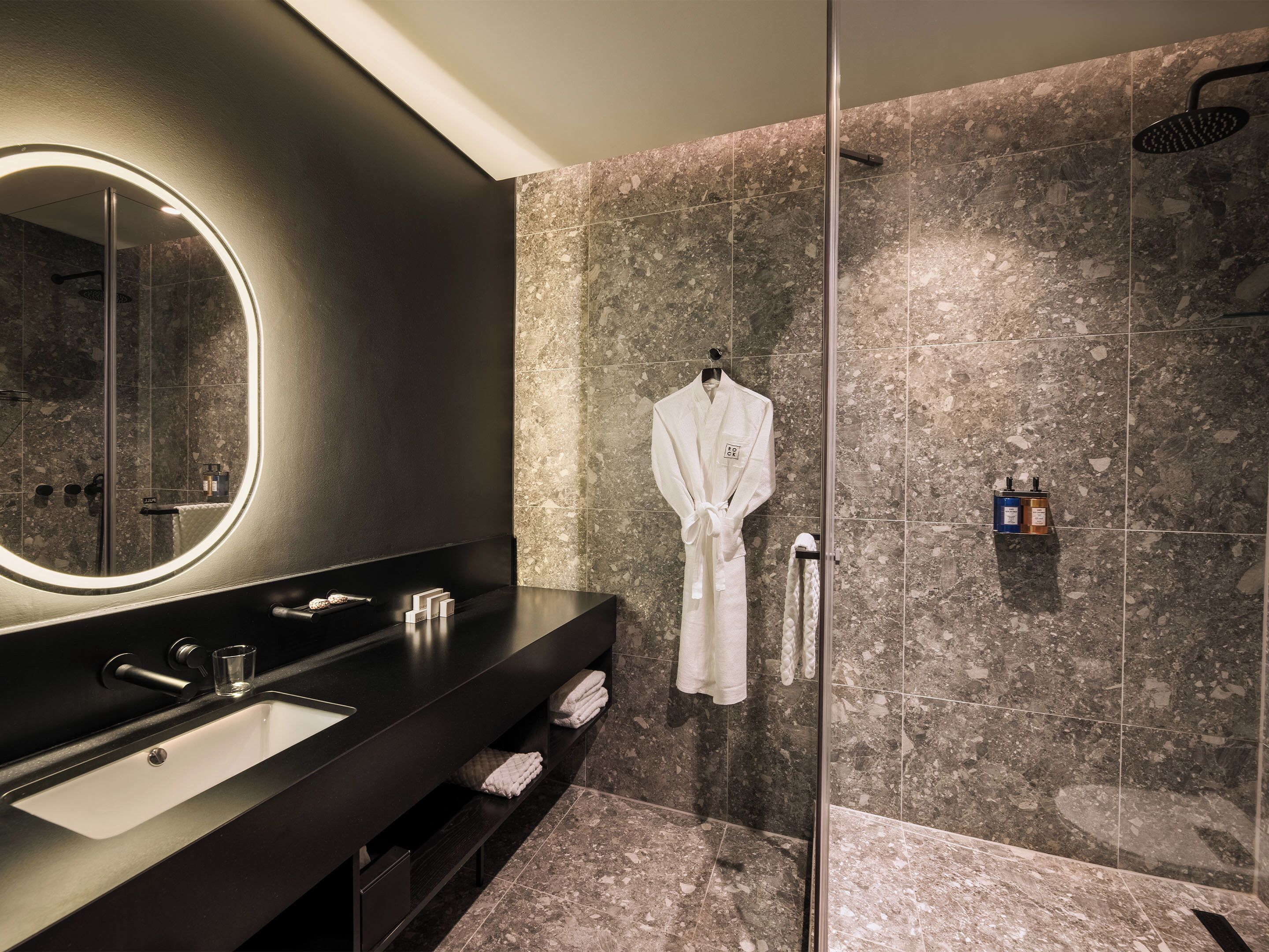 A modern bathroom with a large mirror, a black vanity, a glass-enclosed shower, and marble tiles.