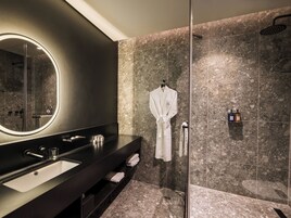 A modern bathroom with a large mirror, a black vanity, a glass-enclosed shower, and marble tiles.
