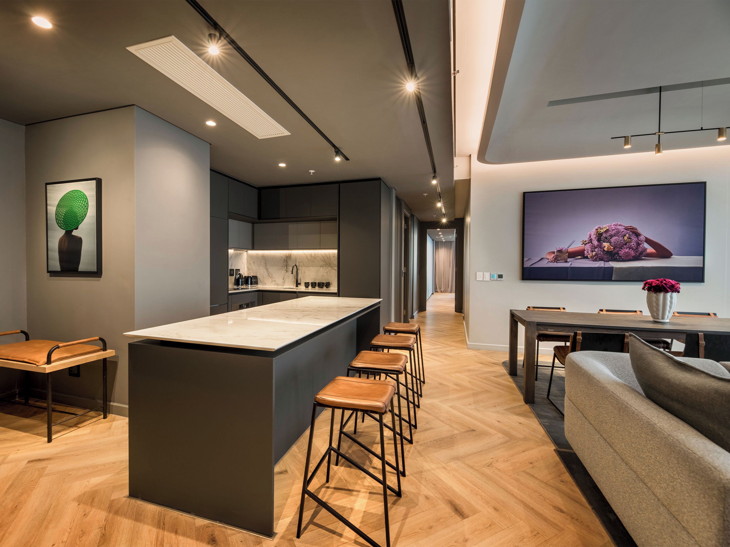 Una cocina moderna con una isla central, taburetes de bar, una zona de comedor con mesa y sillas, y un televisor de pantalla plana grande montado en la pared.