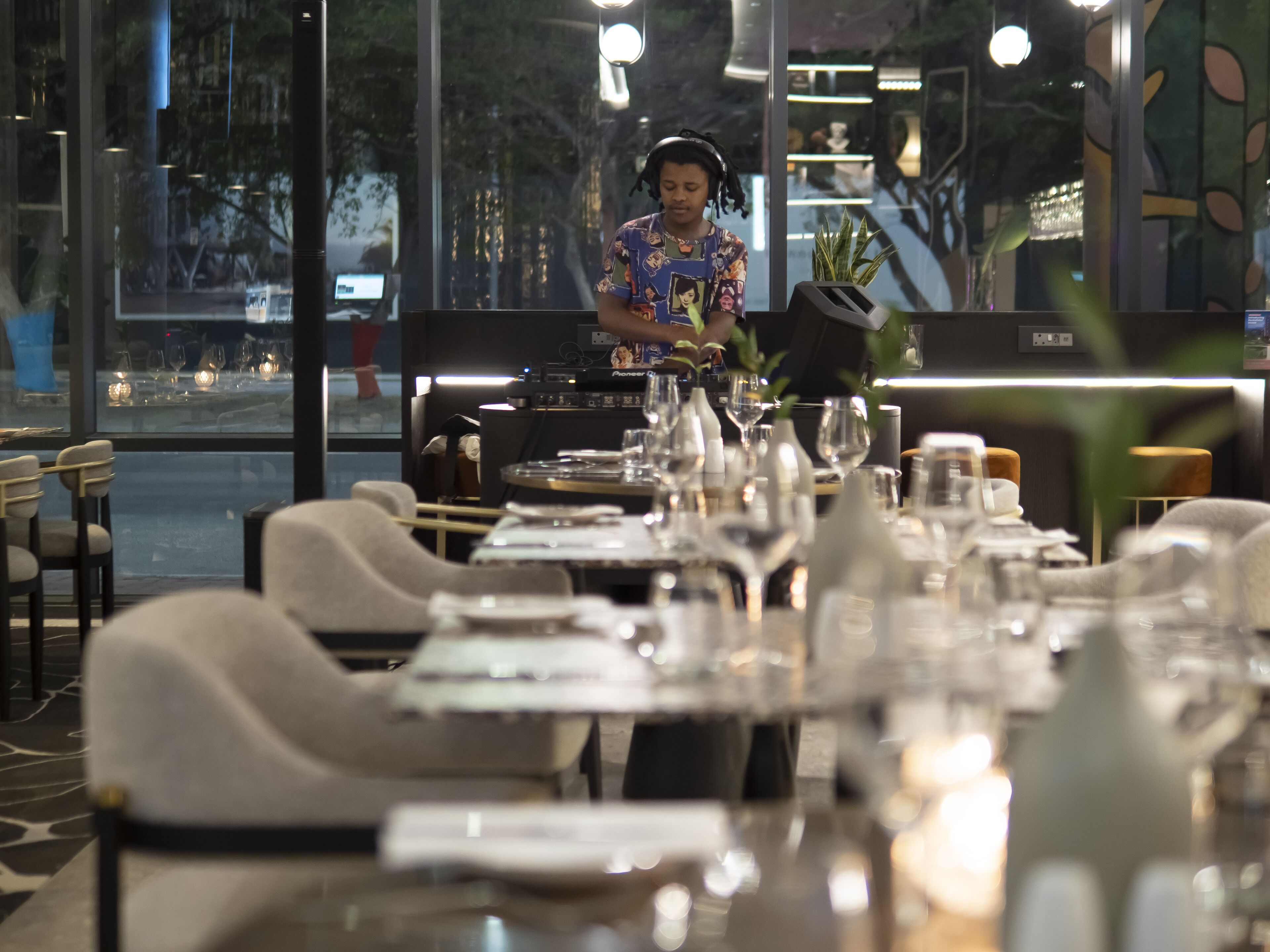 Un restaurant avec des tables dressées pour le service, un barman préparant des boissons et une vue sur la rue.
