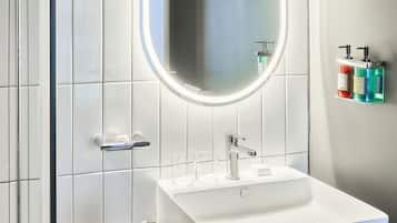 A modern bathroom with a white sink, a mirror with a light, and toiletries on a shelf.