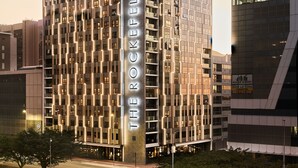 A modern high-rise hotel with a prominent name on its facade, multiple balconies, and a well-lit entrance.