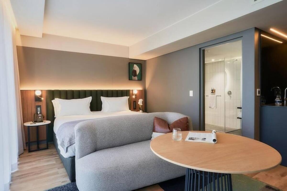 Ein modernes Hotelzimmer mit einem Bett, einem Nachttisch und einem runden Tisch mit einer Fernbedienung.