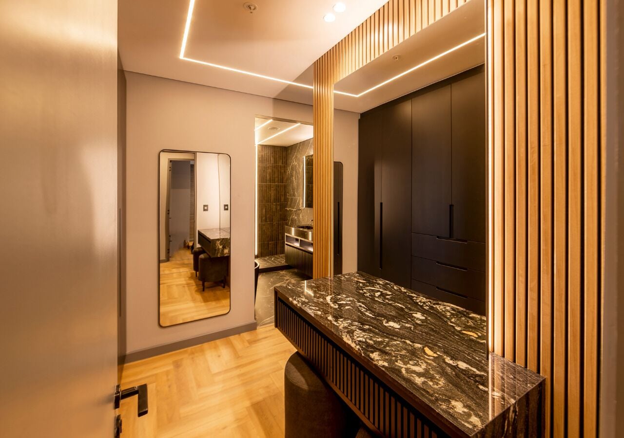 A modern bathroom with a marble countertop, wooden paneling, and a large mirror.