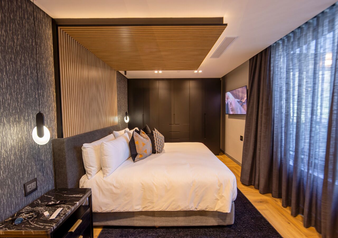 Une chambre d’hôtel moderne avec un grand lit, une table de chevet, une lampe fixée au mur et une vue sur l’extérieur par une fenêtre.