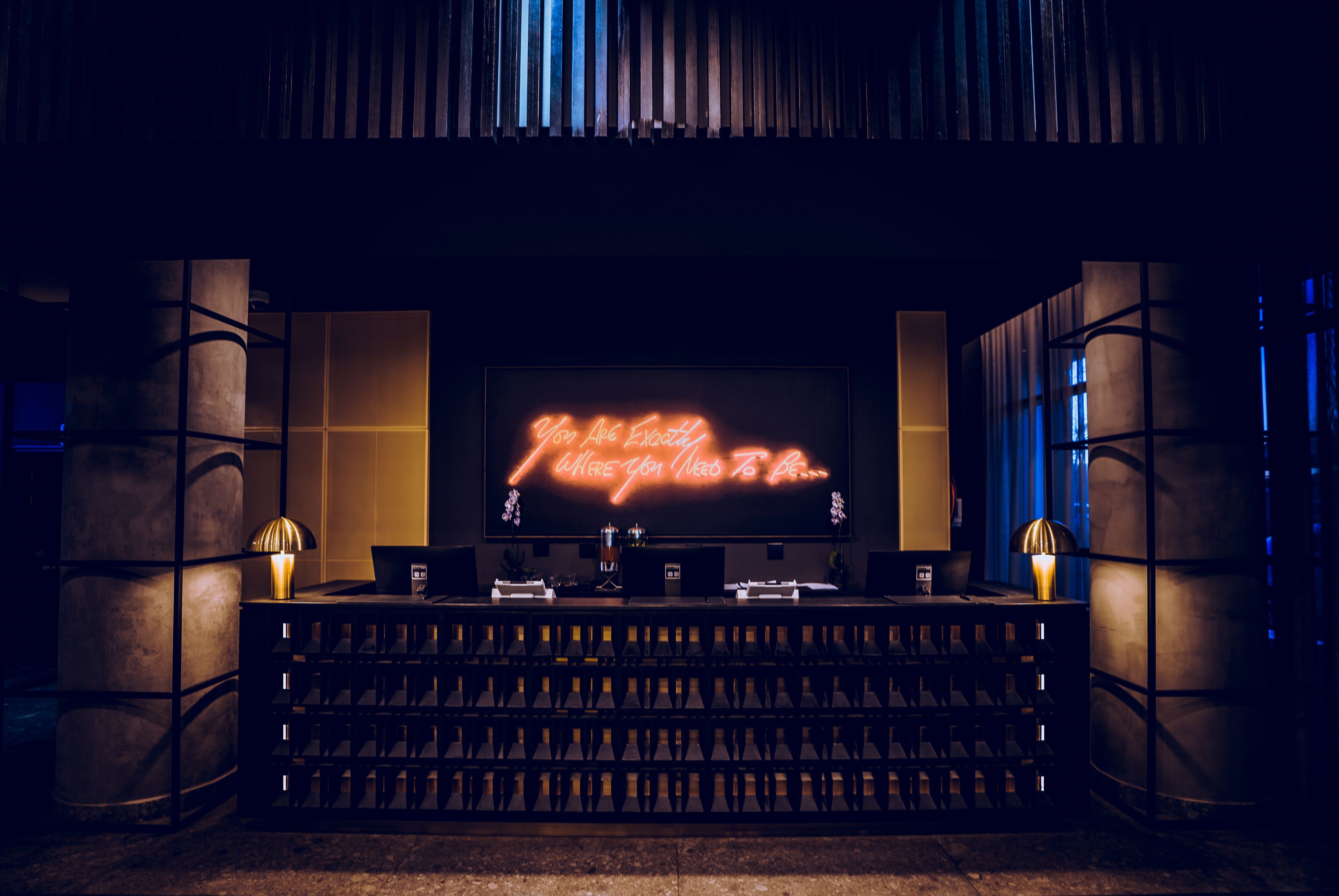 A bar area with a neon sign, bar stools, and a wine rack.