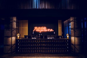 A bar area with a neon sign, bar stools, and a wine rack.