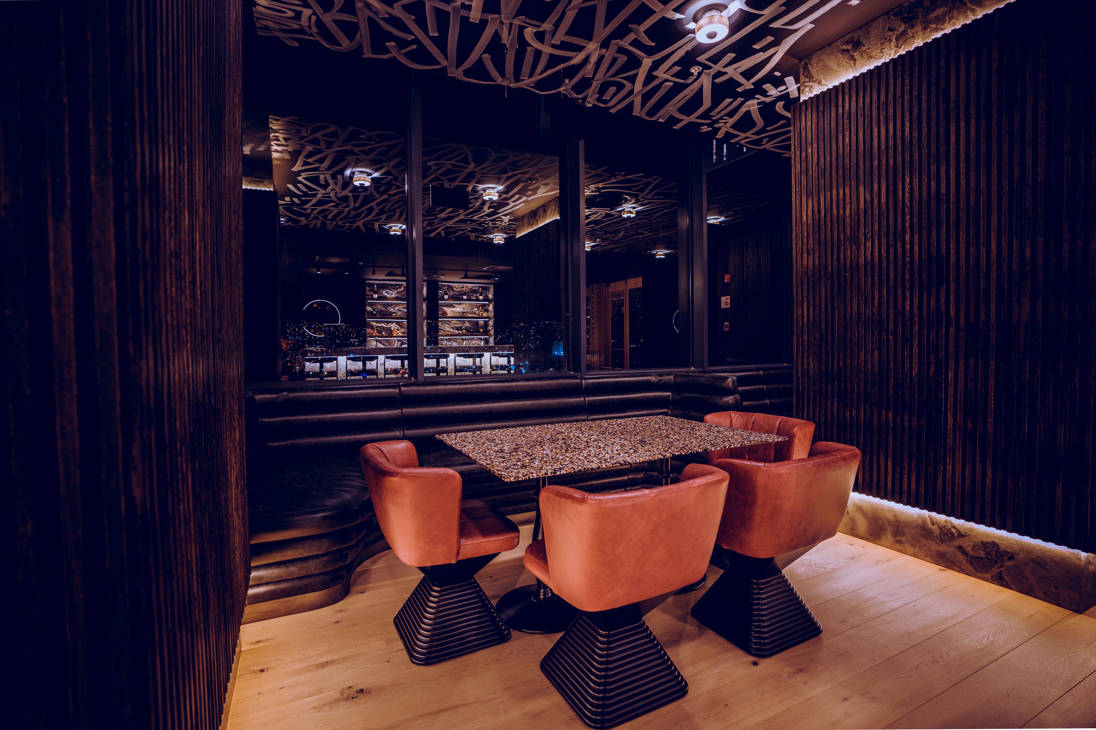 Un interior moderno con piso de madera, una mesa central con cuatro sillas y un techo con diseño.
