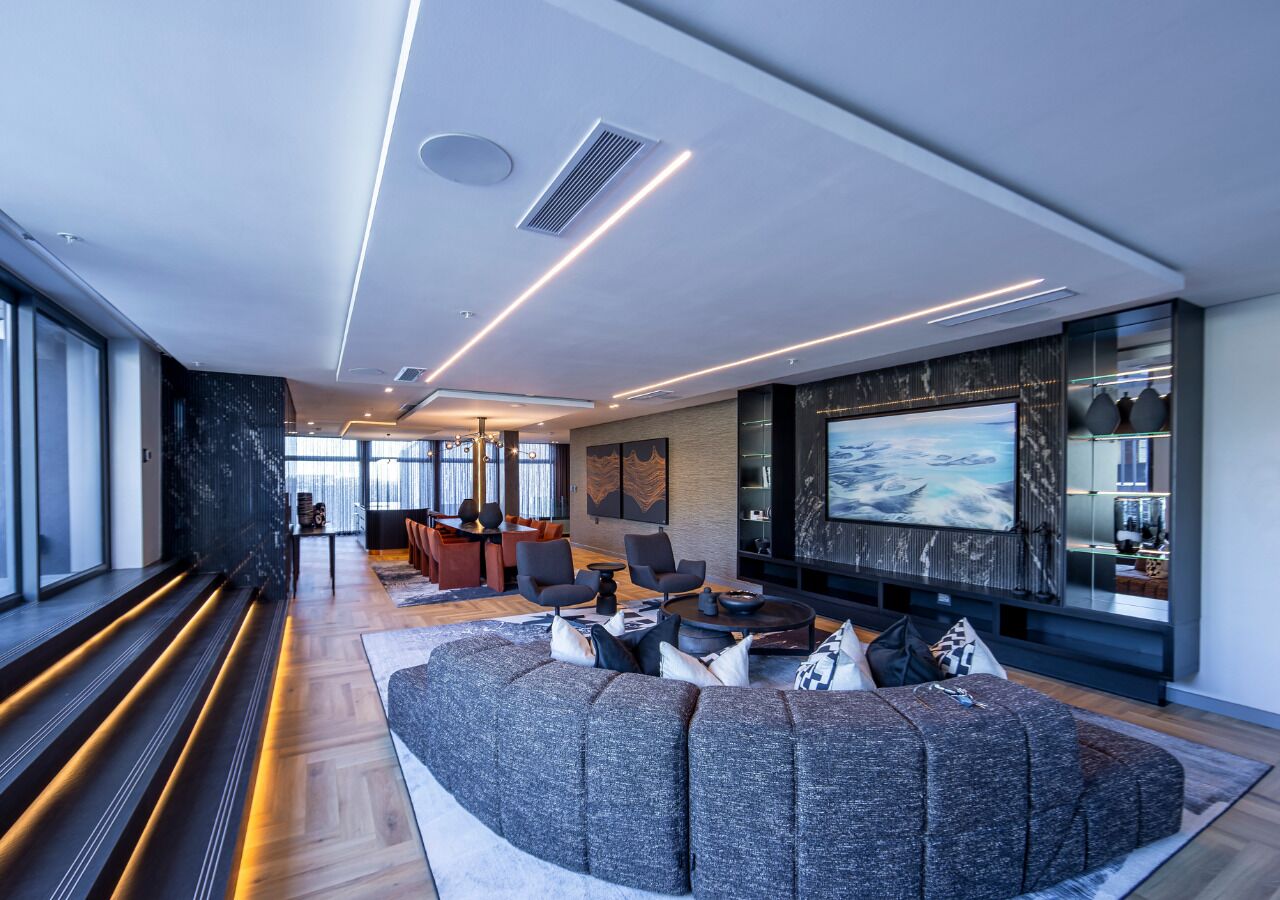 Ein modernes Wohnzimmer mit einem großen Ecksofa, einem Flachbildfernseher und einem Essbereich mit Tisch und Stühlen.