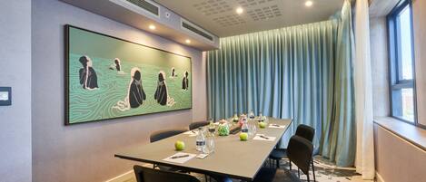 A conference room with a long table, chairs, a large painting, and a window with curtains.