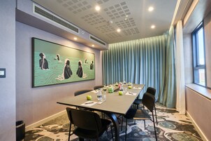 A conference room with a long table, chairs, a large painting, and a window with curtains.