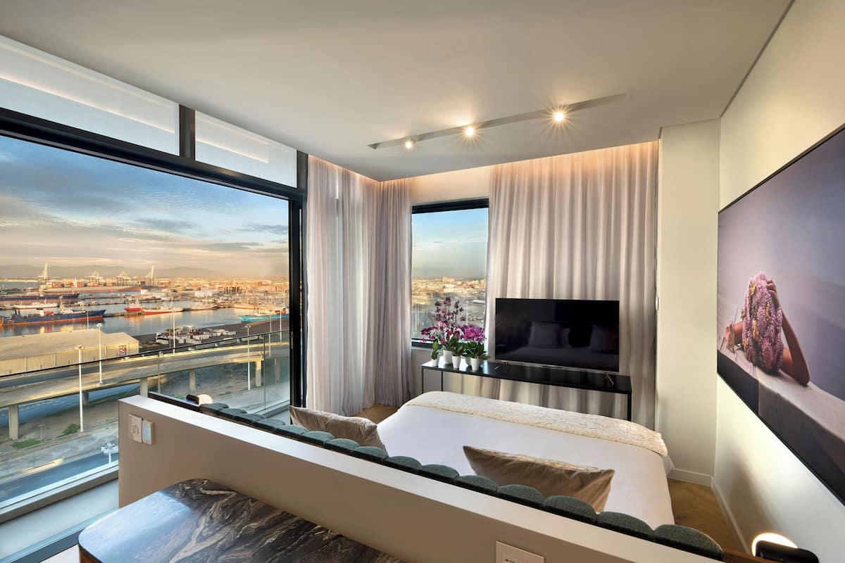 Ein modernes Hotelzimmer mit großem Fenster und Blick auf die Stadt, einem Bett mit Ausblick, einem Flachbildfernseher und einem kleinen Tisch.