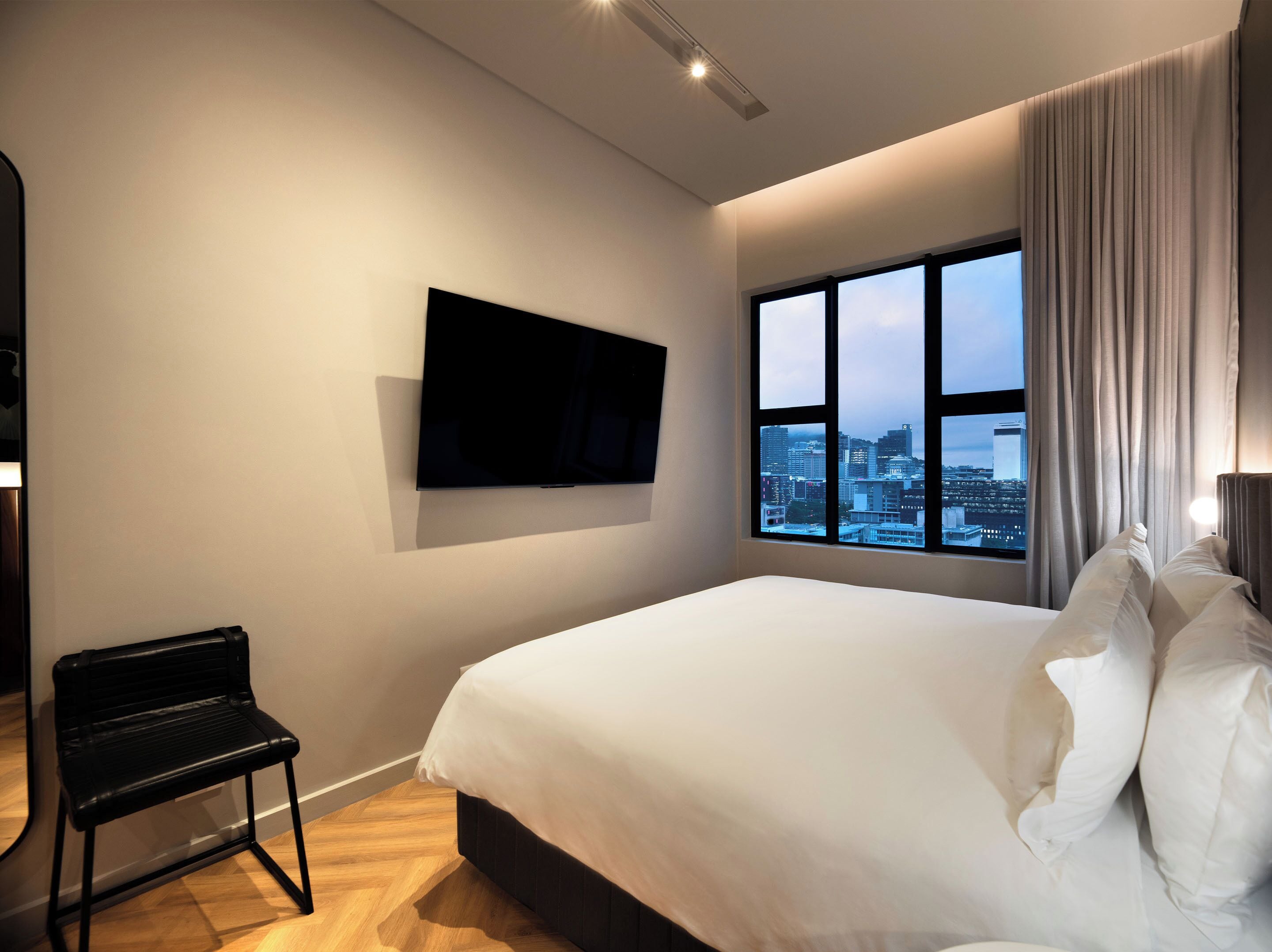 Une chambre d’hôtel dotée d’un grand lit, d’un téléviseur à écran plat fixé au mur, d’un banc et d’une fenêtre donnant sur la ville.