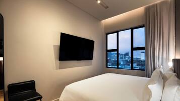 Une chambre d’hôtel dotée d’un grand lit, d’un téléviseur à écran plat fixé au mur, d’un banc et d’une fenêtre donnant sur la ville.