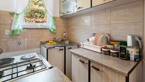 A kitchen with a gas stove, a sink, and a window with a view of greenery. There are cabinets, a countertop, and various kitchen items. - Home Near Red Lake in Ricice (Imotski - Ričice)