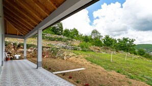 A covered patio with a tiled floor, outdoor seating, and a view of a hilly landscape. - Home Near Red Lake in Ricice (Imotski - Ričice)