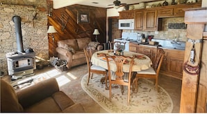 A cozy living room with a stone wall, wooden furniture, a fireplace, and a dining area with a table and chairs. - Loft apartment on Farm with Hot Tub, pond and total privacy.  (Harman)