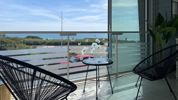 A balcony with a glass door, two black chairs, a small round table, and a view of the sea.