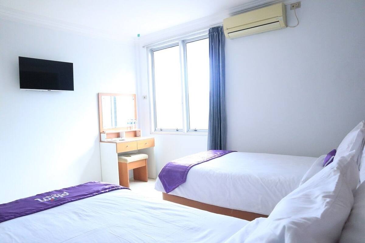 A hotel room with two beds, a desk, a mirror, and a TV.