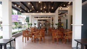 Un área de estar interior con sillas y mesas de madera, techo con vigas y luces a la vista, y un cartel que anuncia un descuento del 25% en comida.