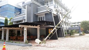 Un hotel con fachada moderna, un área de estar exterior techada y una llamativa escultura inclinada.