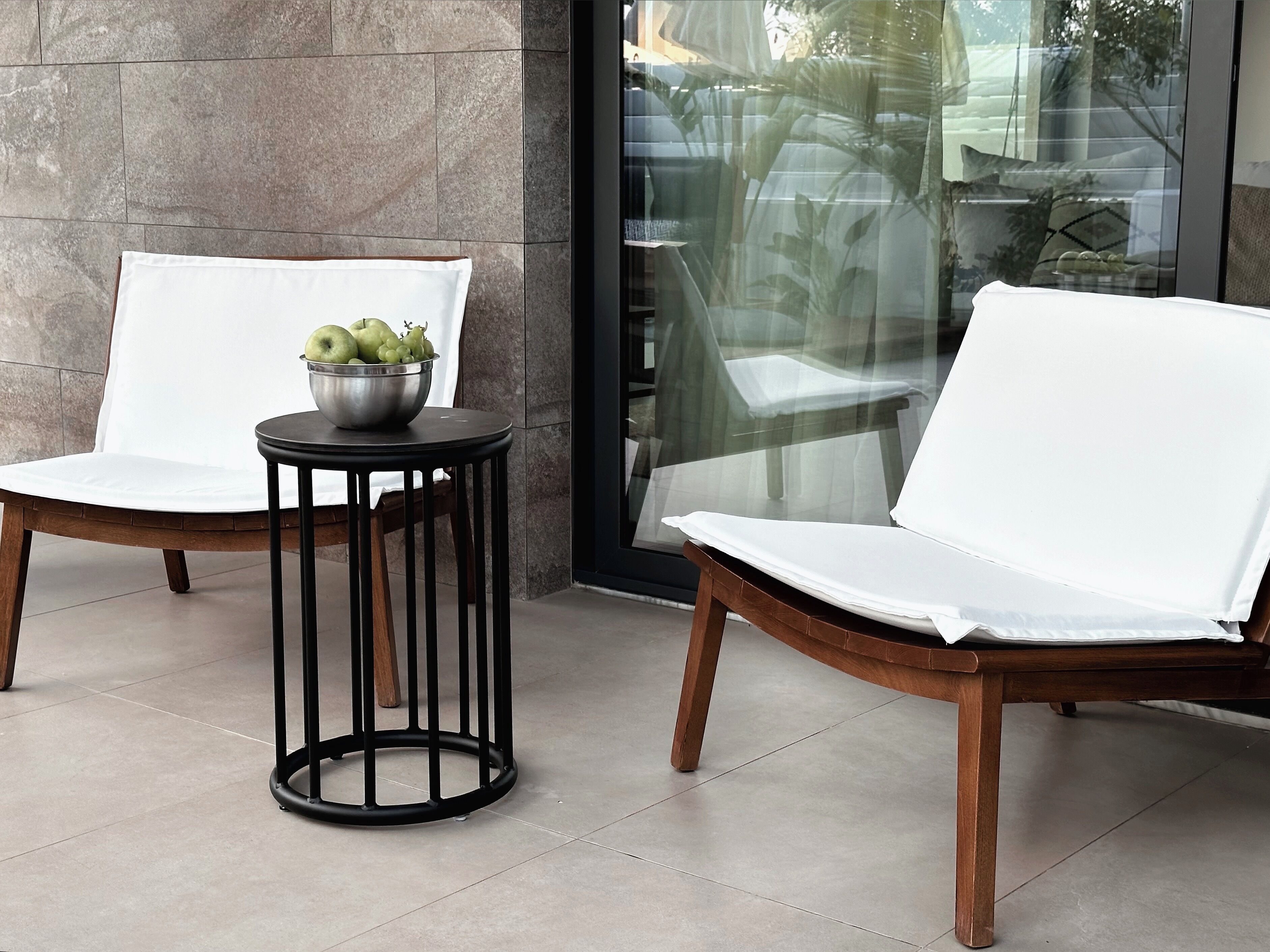 Deux chaises blanches avec des coussins et des pieds en bois, ainsi qu’une petite table ronde avec un pied en métal. Un saladier en métal contenant des pommes vertes et des raisins est posé sur la table.