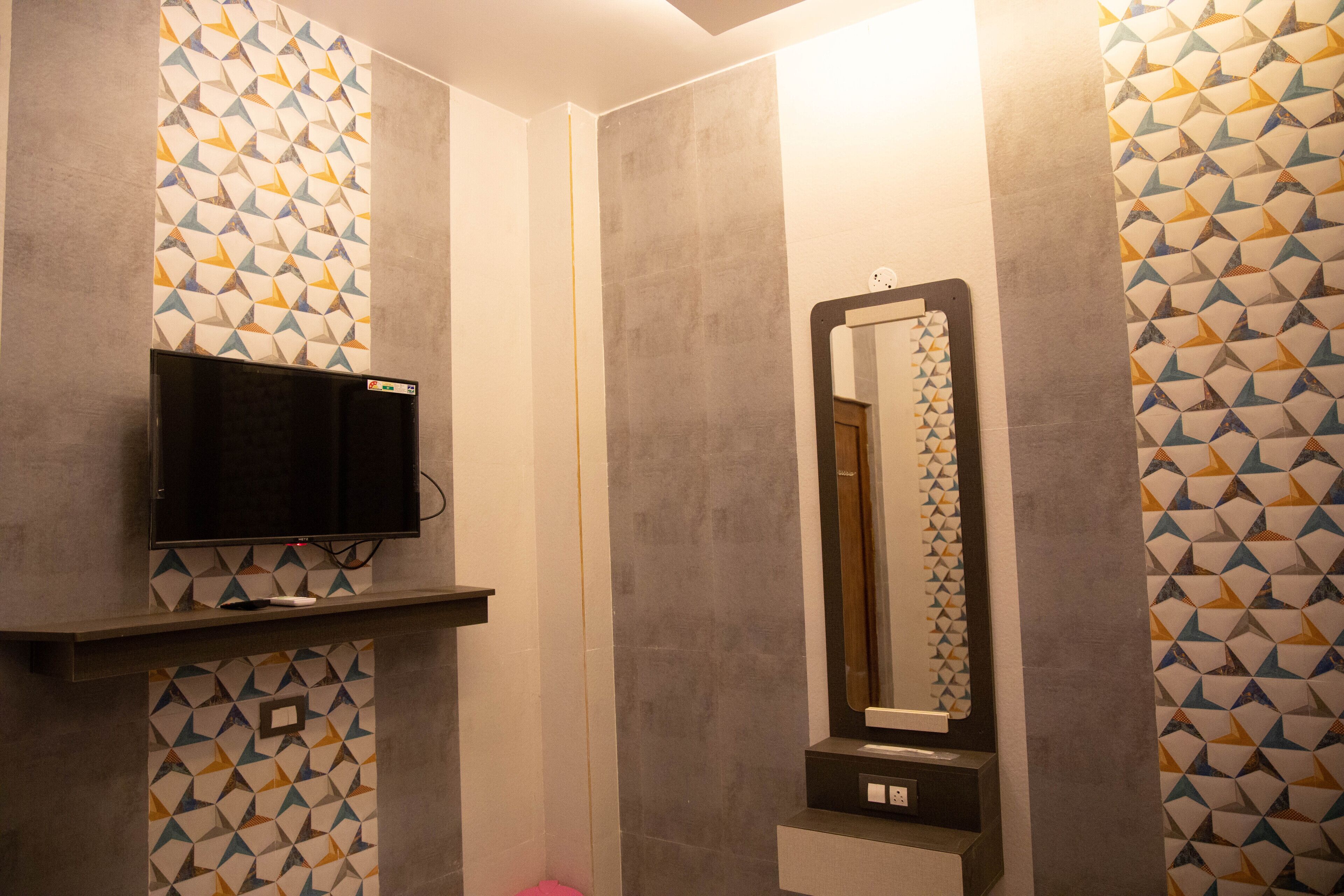 A bathroom with patterned walls, a mirror, a television on a shelf, and a toilet.