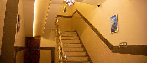Una escalera con escalones de mármol, una puerta de madera y un candelabro en el techo.