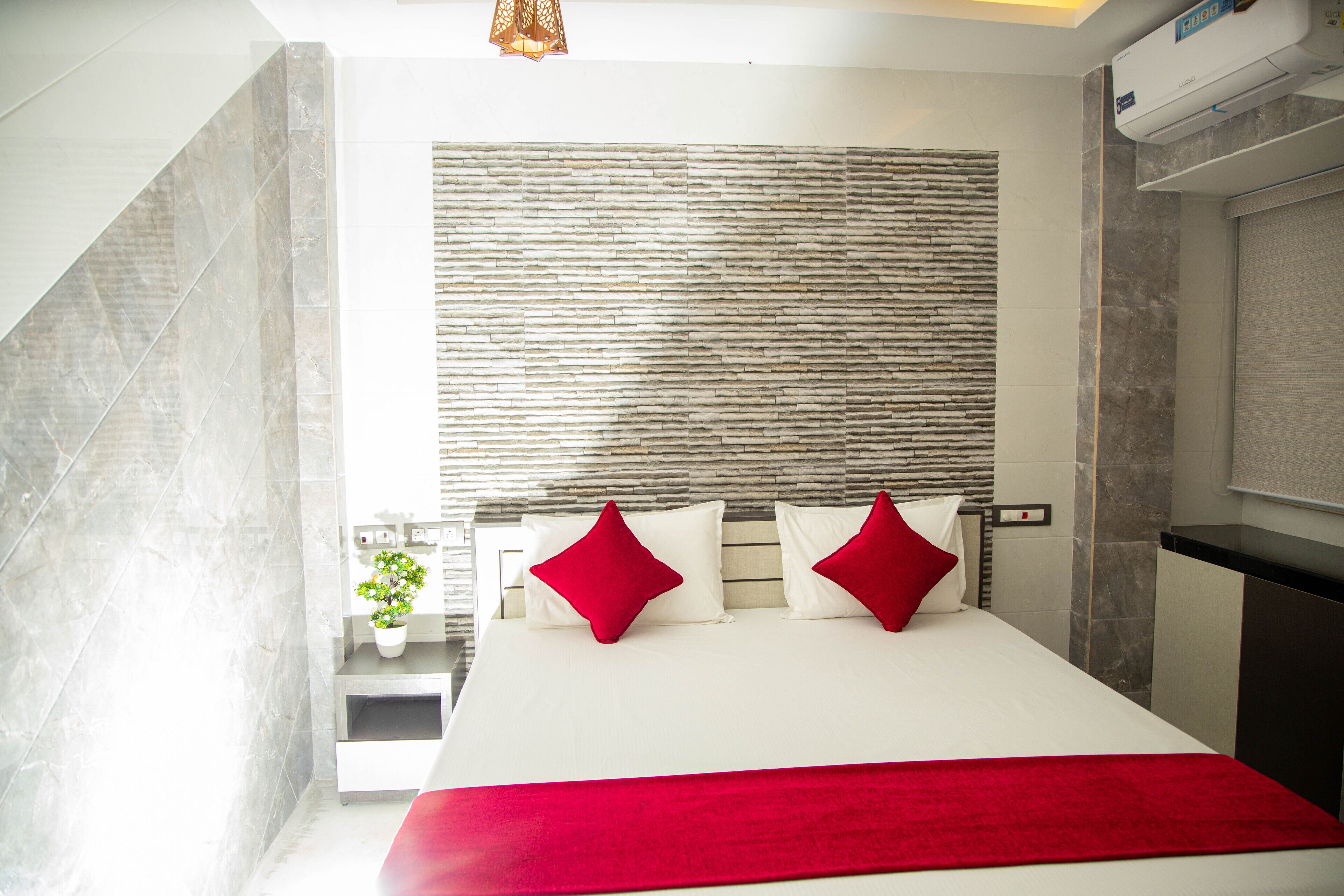 A modern hotel room with a large bed, a stone-textured headboard, a small potted plant, and a red throw blanket.