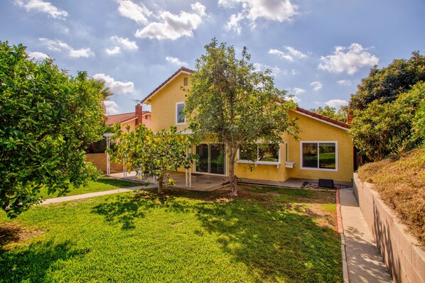 Ein gelbes Haus mit rotem Dach, umgeben von grünem Gras und Bäumen.