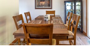 A dining room with a wooden table and chairs, a framed picture on the wall, and a cabinet with glass doors. - Ranch Home w/ Rolling Hill Views & Hot Tub (Harman)